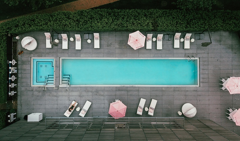 Aerial shot of a long, narrow pool surrounded by sunbeds and pink umbrellas.