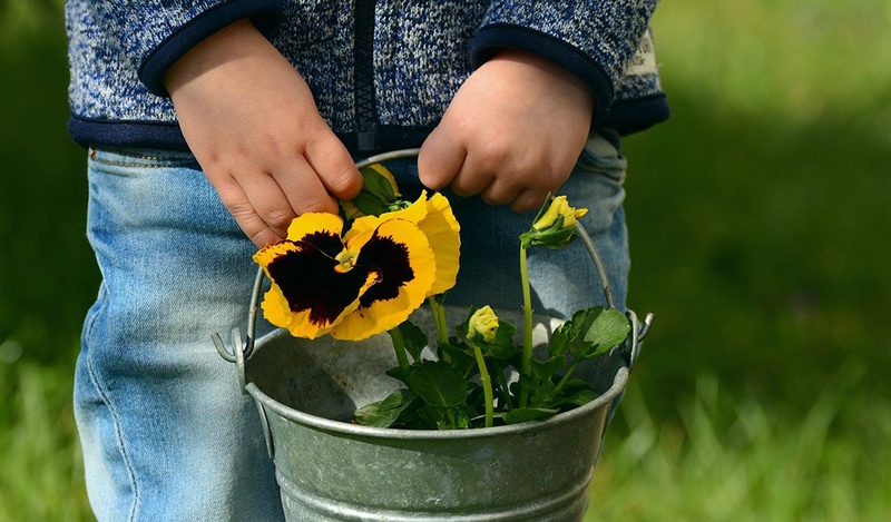 A child holding a bucket with yellow flowers.