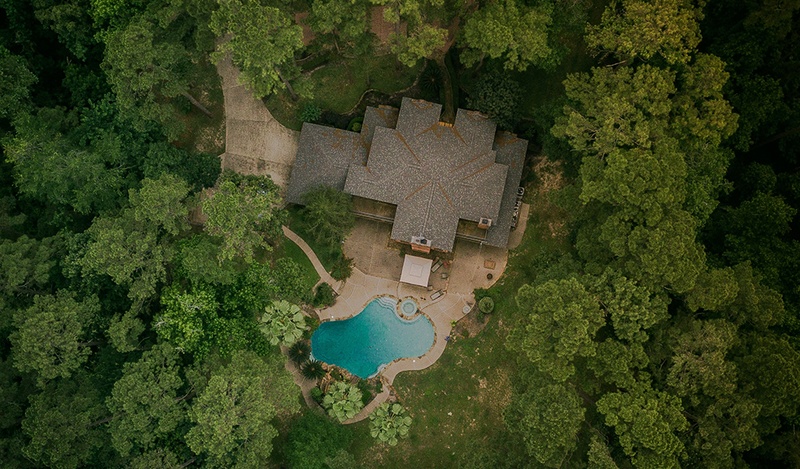 Aerial shot of a house in the middle of the forest with an organically shaped pool.